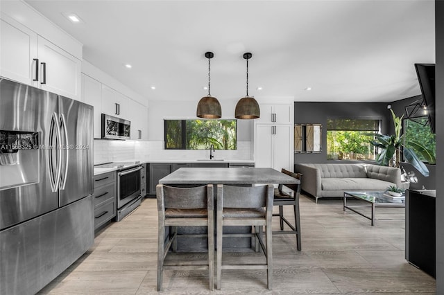 kitchen featuring light hardwood / wood-style flooring, white cabinets, stainless steel appliances, tasteful backsplash, and pendant lighting