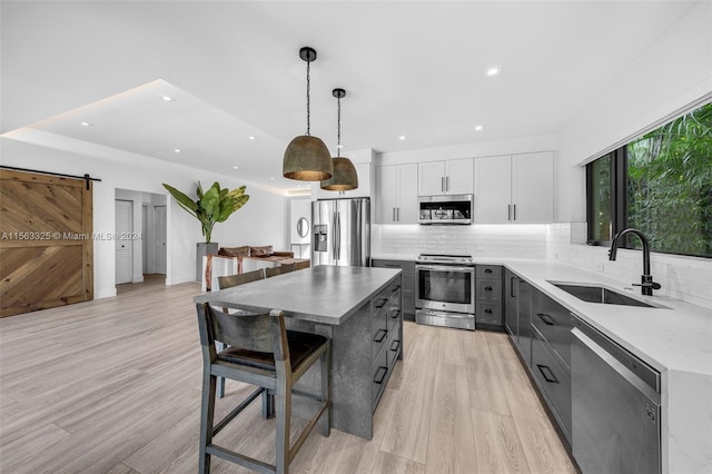 kitchen featuring stainless steel appliances, sink, a barn door, decorative backsplash, and light wood-type flooring