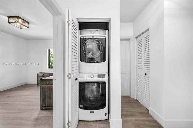 laundry area featuring laundry area, wood finished floors, baseboards, and stacked washing maching and dryer