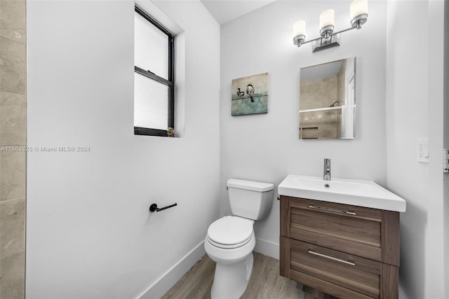 bathroom with baseboards, toilet, wood finished floors, vanity, and a shower