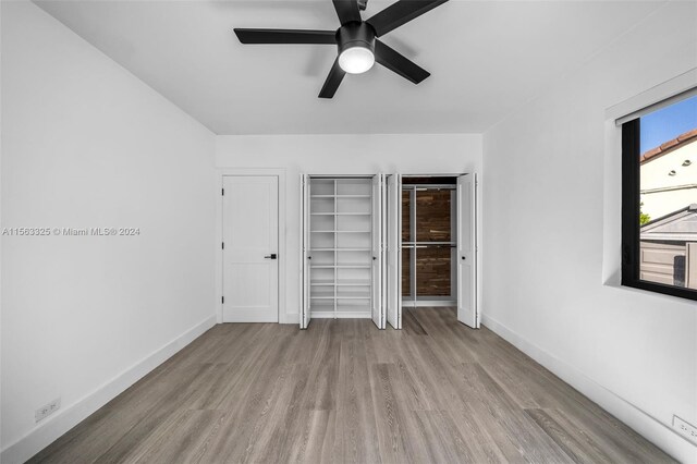 unfurnished bedroom featuring multiple closets, a ceiling fan, baseboards, and wood finished floors