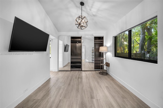 interior space with a notable chandelier, wood finished floors, stairway, baseboards, and vaulted ceiling