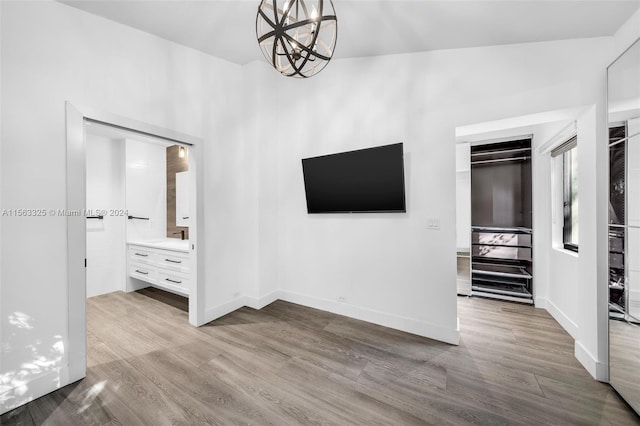 unfurnished bedroom featuring ensuite bath, an inviting chandelier, wood finished floors, and baseboards