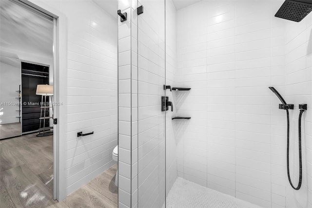 bathroom with toilet, wood finished floors, and a tile shower