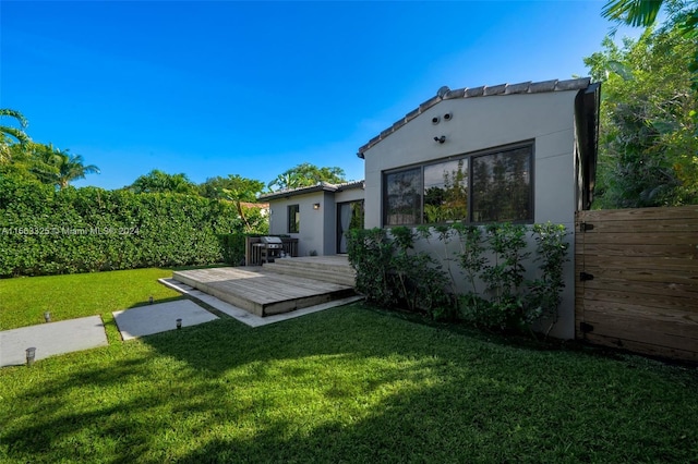 rear view of house with fence, a tiled roof, stucco siding, a lawn, and a deck