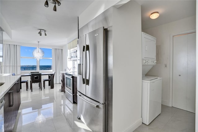 kitchen featuring appliances with stainless steel finishes, a water view, stacked washer / drying machine, decorative light fixtures, and a chandelier