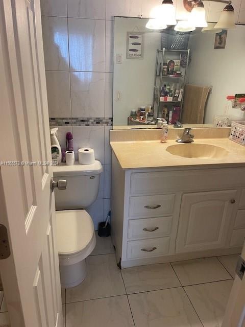 bathroom with toilet, tile flooring, vanity, and tile walls