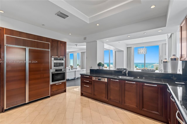 kitchen featuring paneled appliances, a tray ceiling, sink, an inviting chandelier, and light tile floors