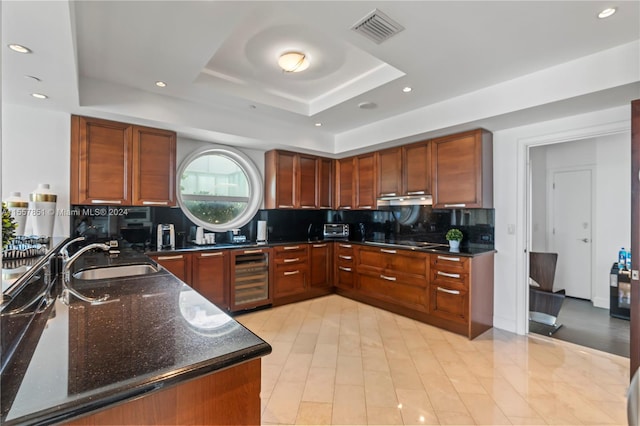 kitchen featuring backsplash, beverage cooler, a tray ceiling, dark stone countertops, and sink