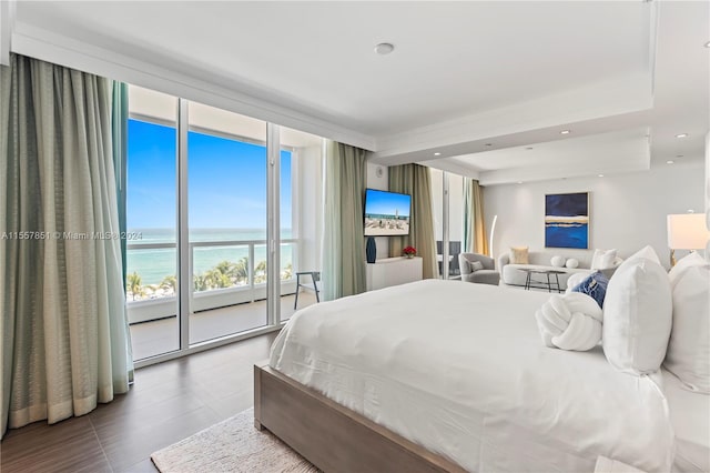 bedroom with a water view, a raised ceiling, tile floors, and access to exterior