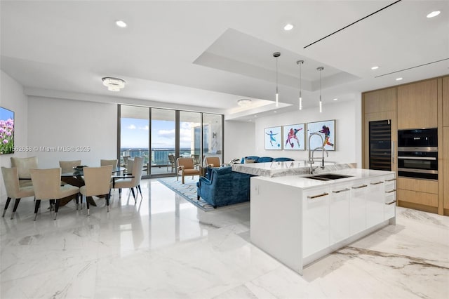 kitchen featuring a tray ceiling, double oven, open floor plan, a sink, and modern cabinets