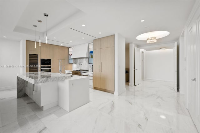 kitchen featuring a kitchen bar, a kitchen island with sink, pendant lighting, premium range hood, and light stone countertops