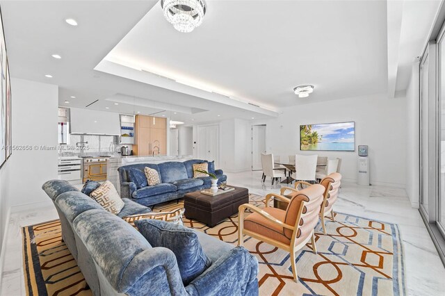 living room with a raised ceiling, a chandelier, and light tile flooring