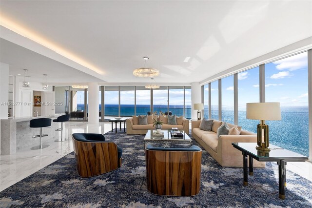 living room featuring a chandelier, floor to ceiling windows, a water view, and a healthy amount of sunlight