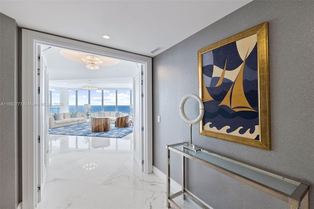 corridor featuring a chandelier, a textured wall, visible vents, baseboards, and marble finish floor