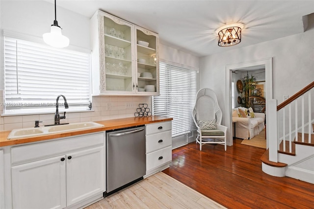 kitchen with light hardwood / wood-style flooring, white cabinets, stainless steel dishwasher, tasteful backsplash, and pendant lighting