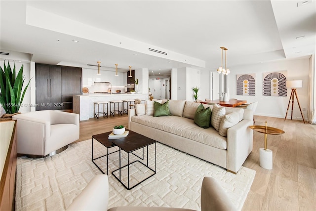 living room featuring light wood-style floors, a tray ceiling, a chandelier, and recessed lighting