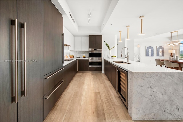 kitchen featuring light wood-style flooring, a sink, modern cabinets, beverage cooler, and a peninsula