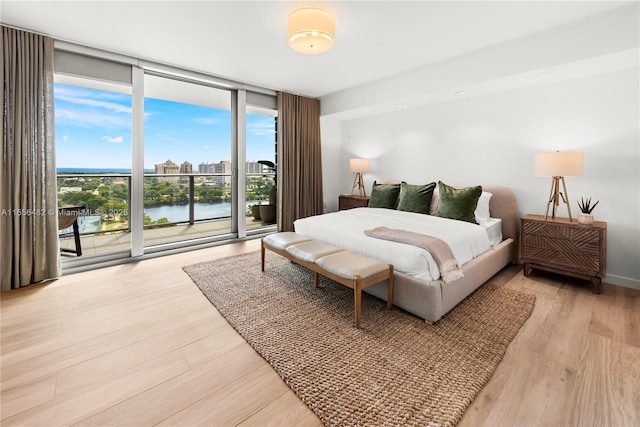 bedroom with baseboards, light wood-style floors, access to outside, a view of city, and a wall of windows