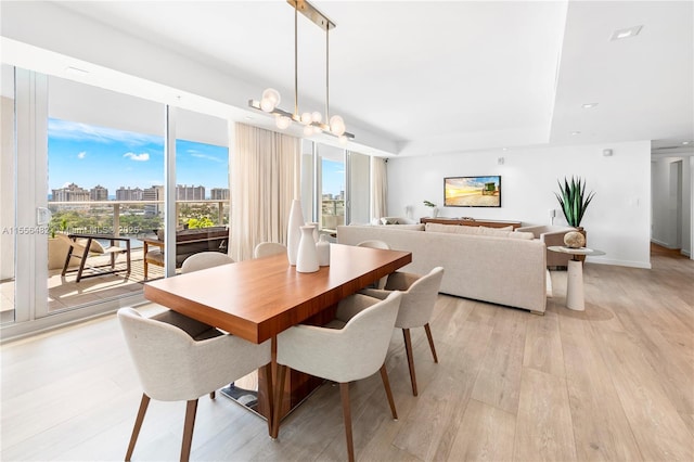 dining space with a notable chandelier, a city view, baseboards, light wood finished floors, and a raised ceiling