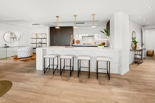 kitchen featuring tasteful backsplash, a kitchen breakfast bar, a peninsula, pendant lighting, and a sink