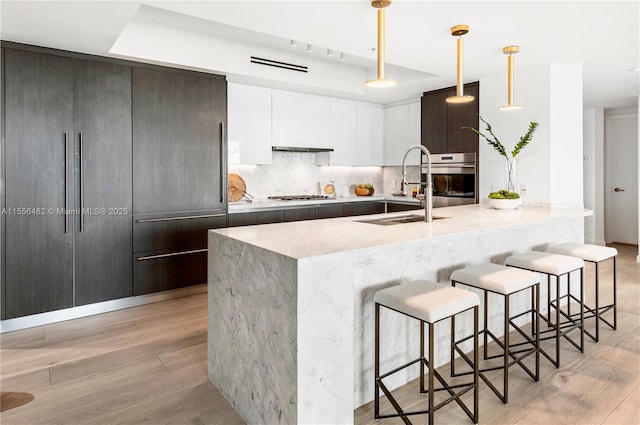 kitchen with tasteful backsplash, light wood-style flooring, appliances with stainless steel finishes, light stone countertops, and a sink