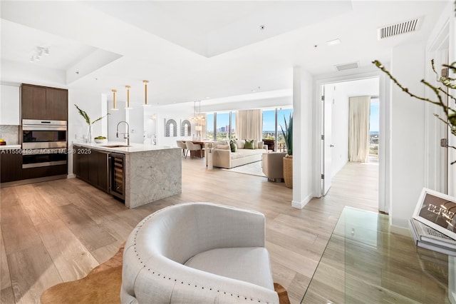 kitchen with wine cooler, a raised ceiling, visible vents, a sink, and dark brown cabinetry