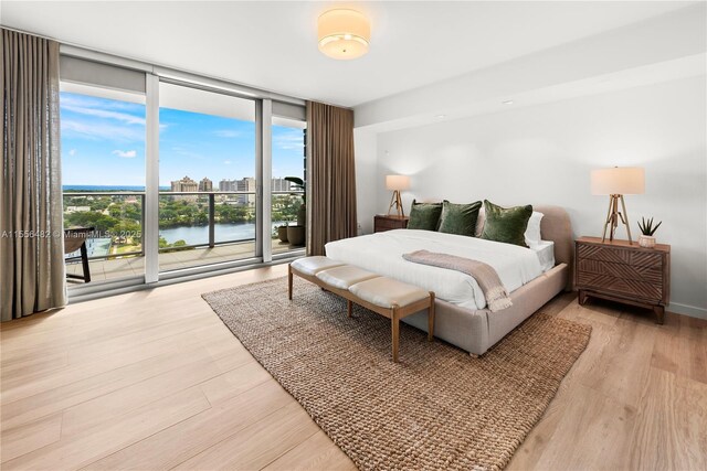 bedroom with access to exterior, a view of city, light wood-style floors, expansive windows, and baseboards