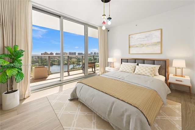 bedroom featuring access to exterior, expansive windows, a city view, and wood finished floors