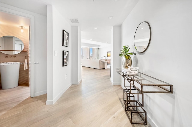 hallway with light wood-type flooring, baseboards, and visible vents