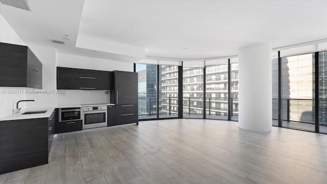 kitchen featuring stainless steel oven, light wood-type flooring, a wall of windows, and sink