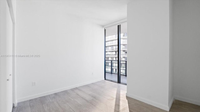 spare room featuring plenty of natural light, expansive windows, and light hardwood / wood-style floors