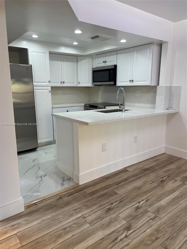 kitchen with kitchen peninsula, appliances with stainless steel finishes, backsplash, light hardwood / wood-style floors, and white cabinetry