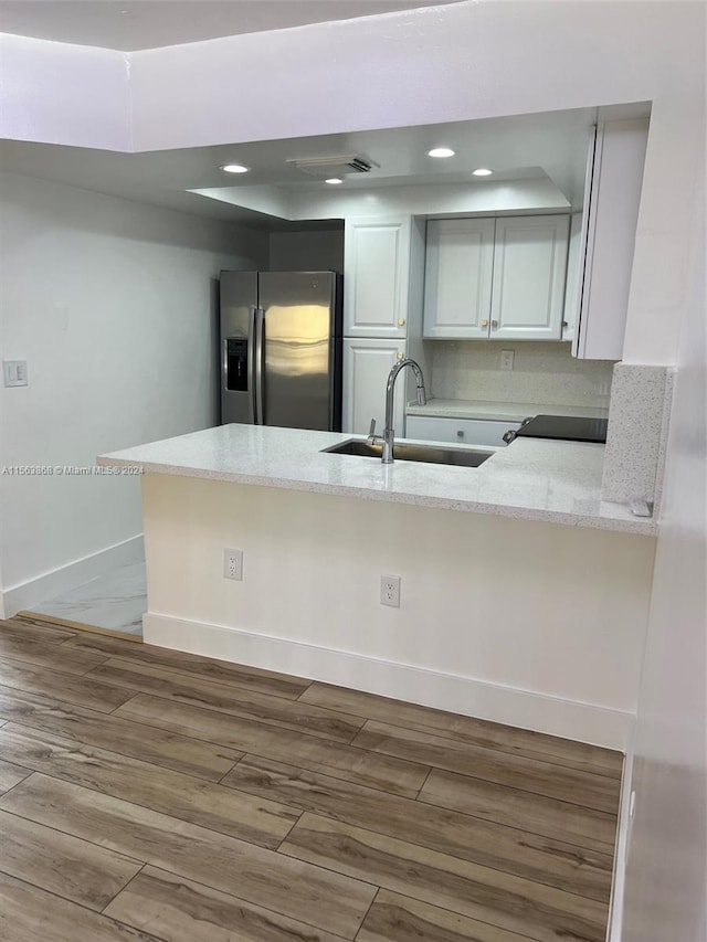 kitchen featuring light hardwood / wood-style floors, kitchen peninsula, stainless steel fridge with ice dispenser, white cabinets, and sink