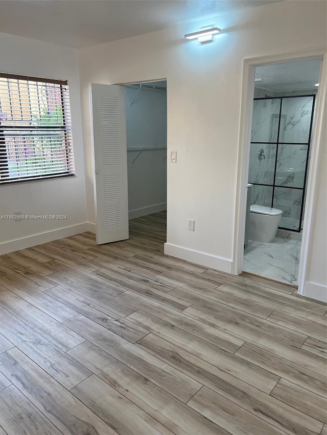 unfurnished bedroom featuring a walk in closet, a closet, ensuite bathroom, and light wood-type flooring