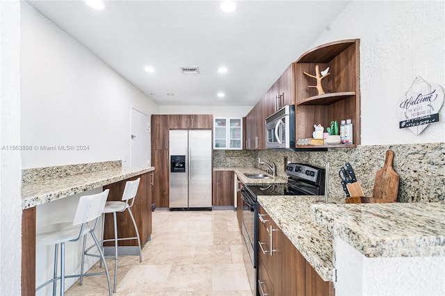 kitchen with sink, light tile floors, stainless steel appliances, light stone countertops, and a kitchen bar