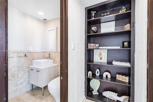 bathroom featuring toilet, tile flooring, vanity, and tile walls