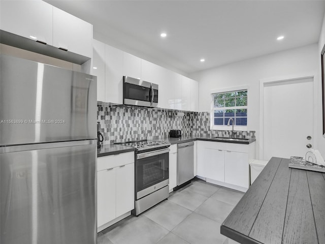 kitchen with stainless steel appliances, light tile floors, tasteful backsplash, white cabinets, and sink