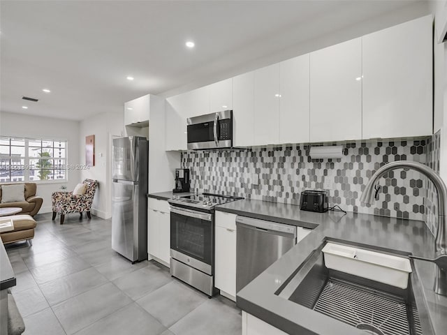 kitchen with stainless steel appliances, backsplash, light tile floors, sink, and white cabinets