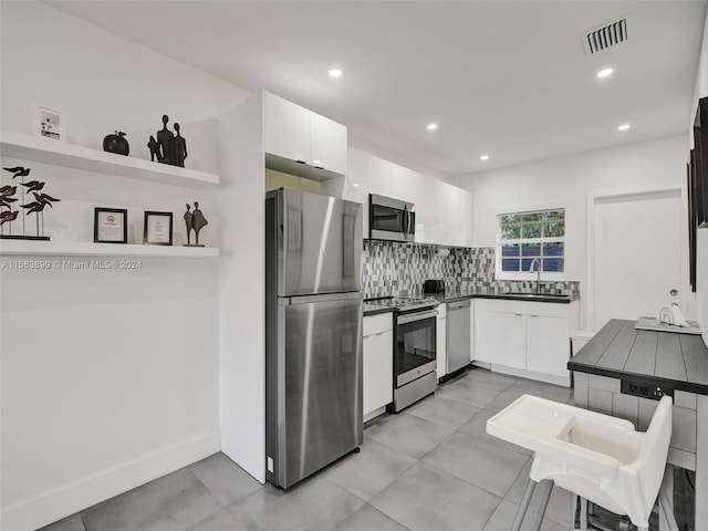 kitchen with backsplash, white cabinetry, appliances with stainless steel finishes, and light tile floors