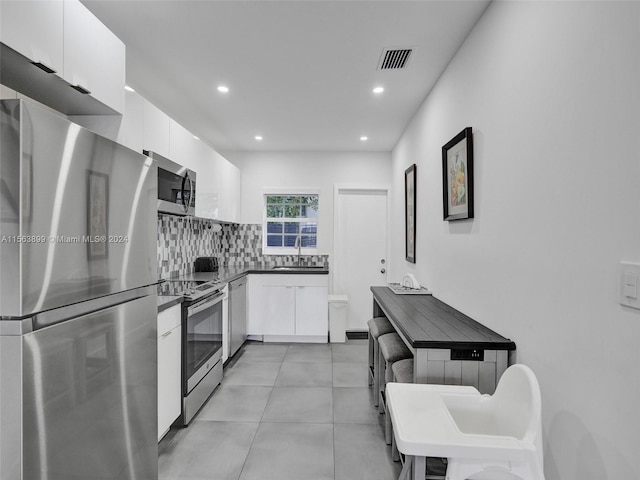 kitchen with light tile flooring, tasteful backsplash, stainless steel appliances, sink, and white cabinets