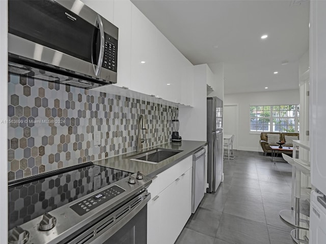 kitchen with sink, backsplash, stainless steel appliances, tile floors, and white cabinetry