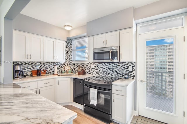 kitchen featuring white cabinets, backsplash, light wood-type flooring, black appliances, and a sink