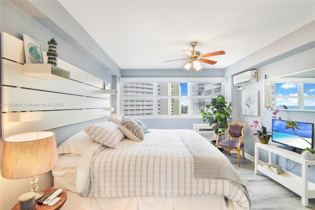 bedroom featuring a wall unit AC, wood finished floors, a ceiling fan, baseboards, and an AC wall unit