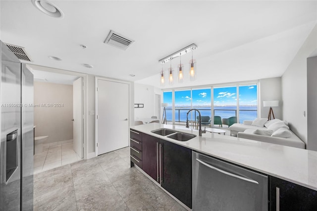 kitchen with a water view, dishwasher, sink, light tile floors, and pendant lighting