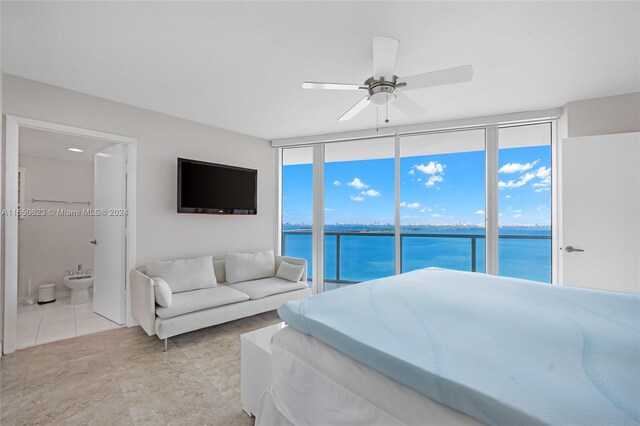 tiled bedroom featuring ceiling fan, access to outside, a water view, ensuite bath, and multiple windows