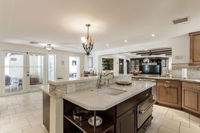 kitchen featuring a chandelier, french doors, a center island with sink, pendant lighting, and sink