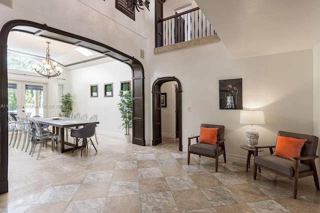 interior space featuring a towering ceiling, light tile floors, french doors, and an inviting chandelier