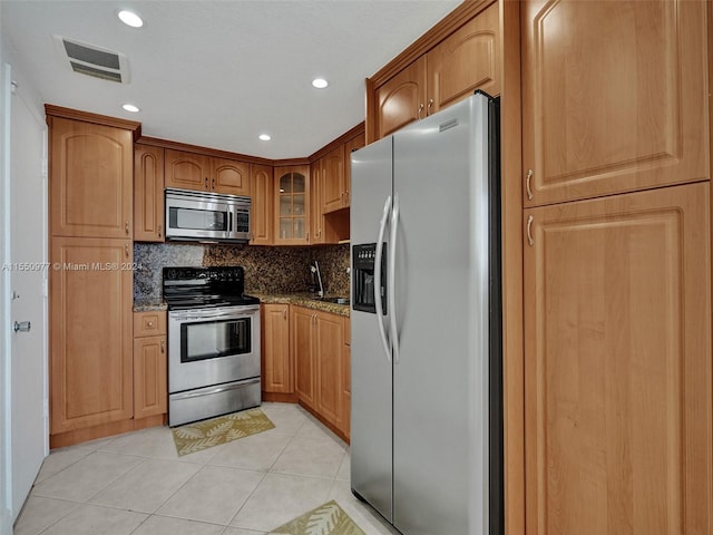 kitchen with appliances with stainless steel finishes, light tile flooring, tasteful backsplash, and light stone countertops