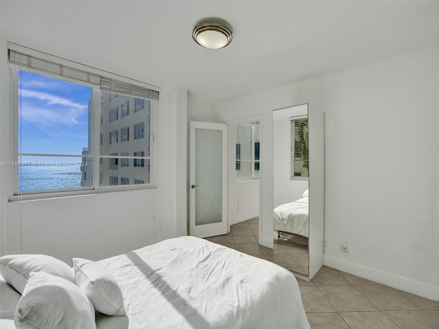 bedroom with a water view, light tile floors, and french doors